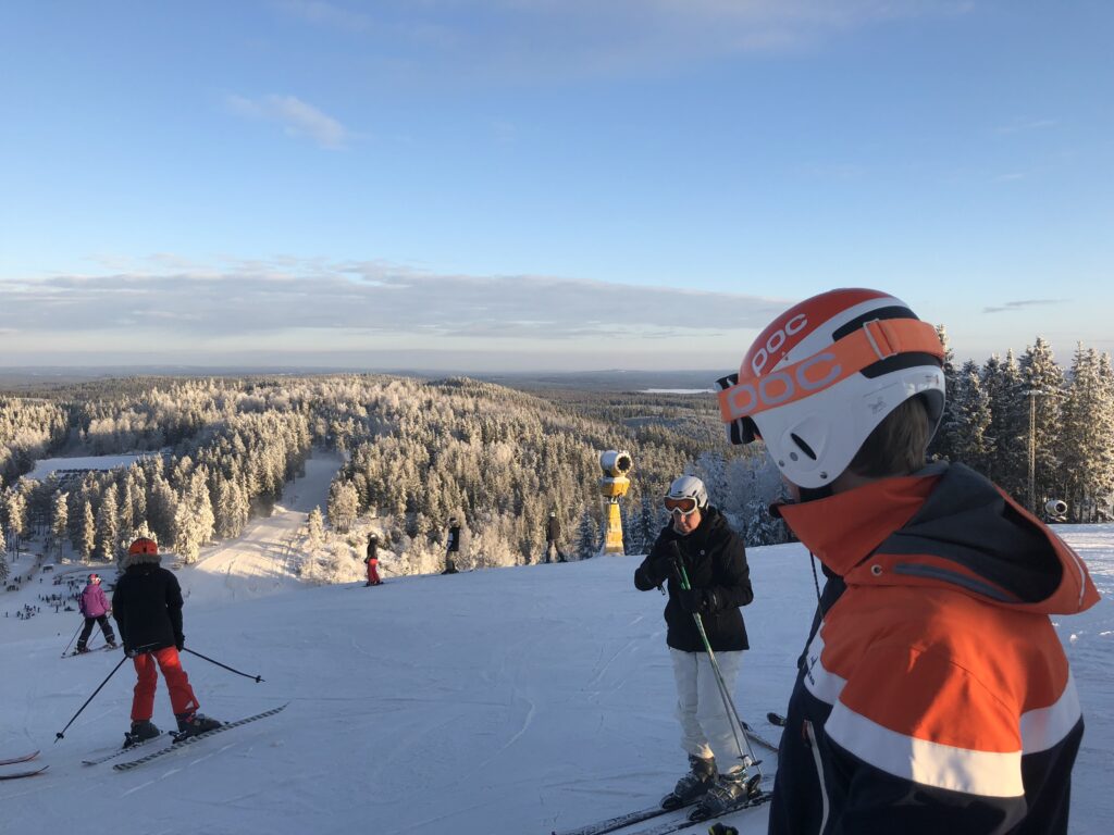 Skidåkare på toppen av Isaberg i Hestra ser ut över skidbackarna en solig vinterdag, med vidsträckt utsikt över Smålands landskap.