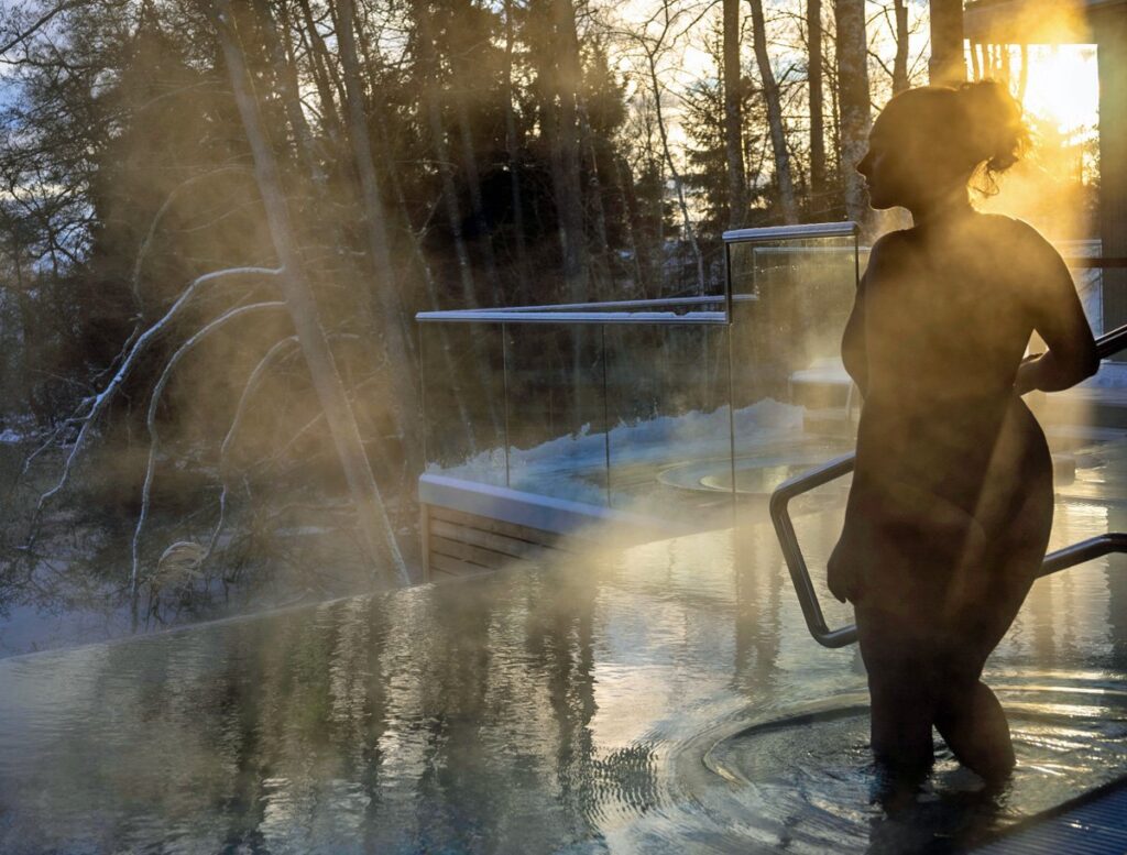 Tjej som njuter av ett dopp i de varma poolerna med solnedgång i bakgrunden.