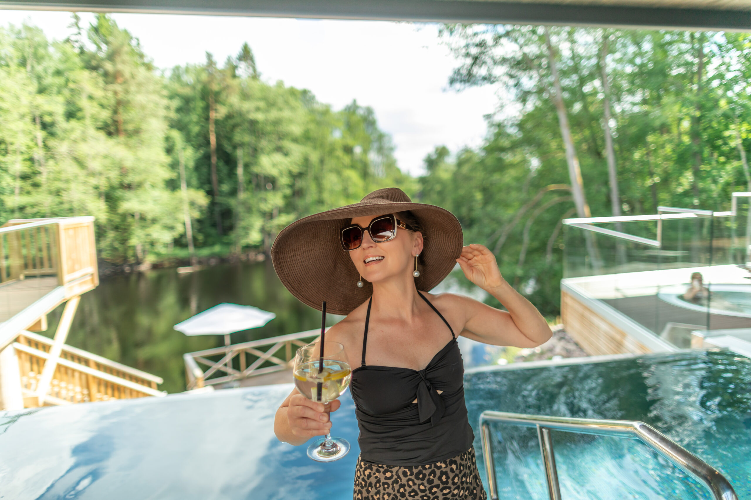 Kvinna i poolen på Hestraviken, med utsikt över Nissan och en drink i handen under midsommarlunchen.