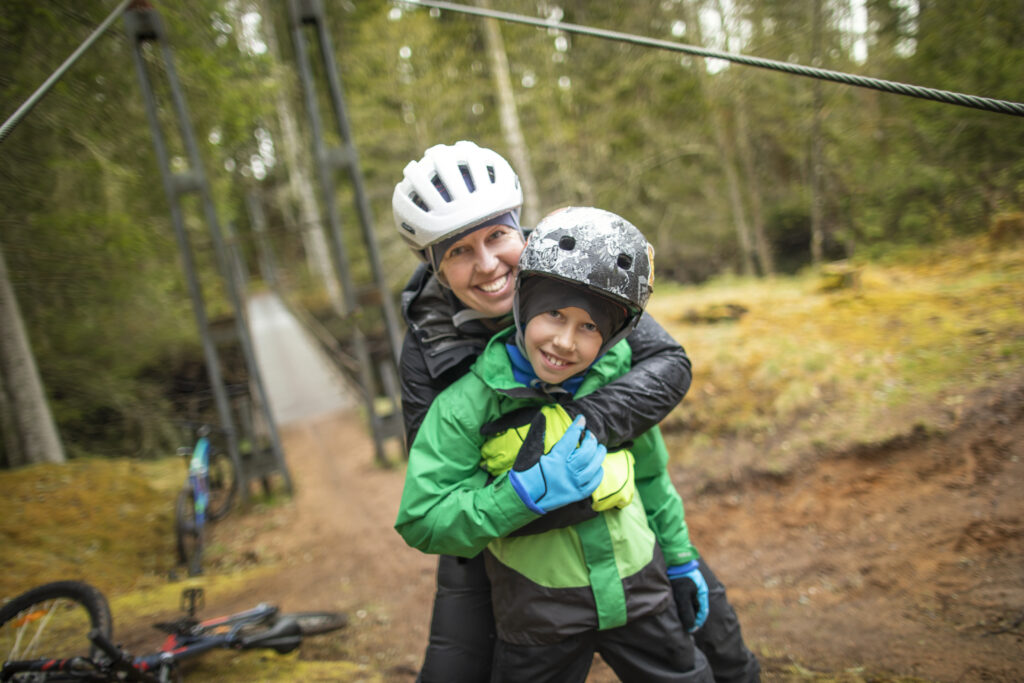 Mamma och son kramas under cykelturen mellan Hestraviken och Isaberg. I bakgrunden ser man cykelbron över Nissan vid Nissaforsbruk