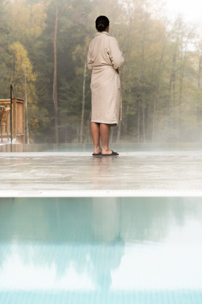 Tjej på terrassen i Riverside Spa på Hestraviken hotell vid Isaberg, blickar ut över Nissan och poolerna, en avkopplande morgonupplevelse.