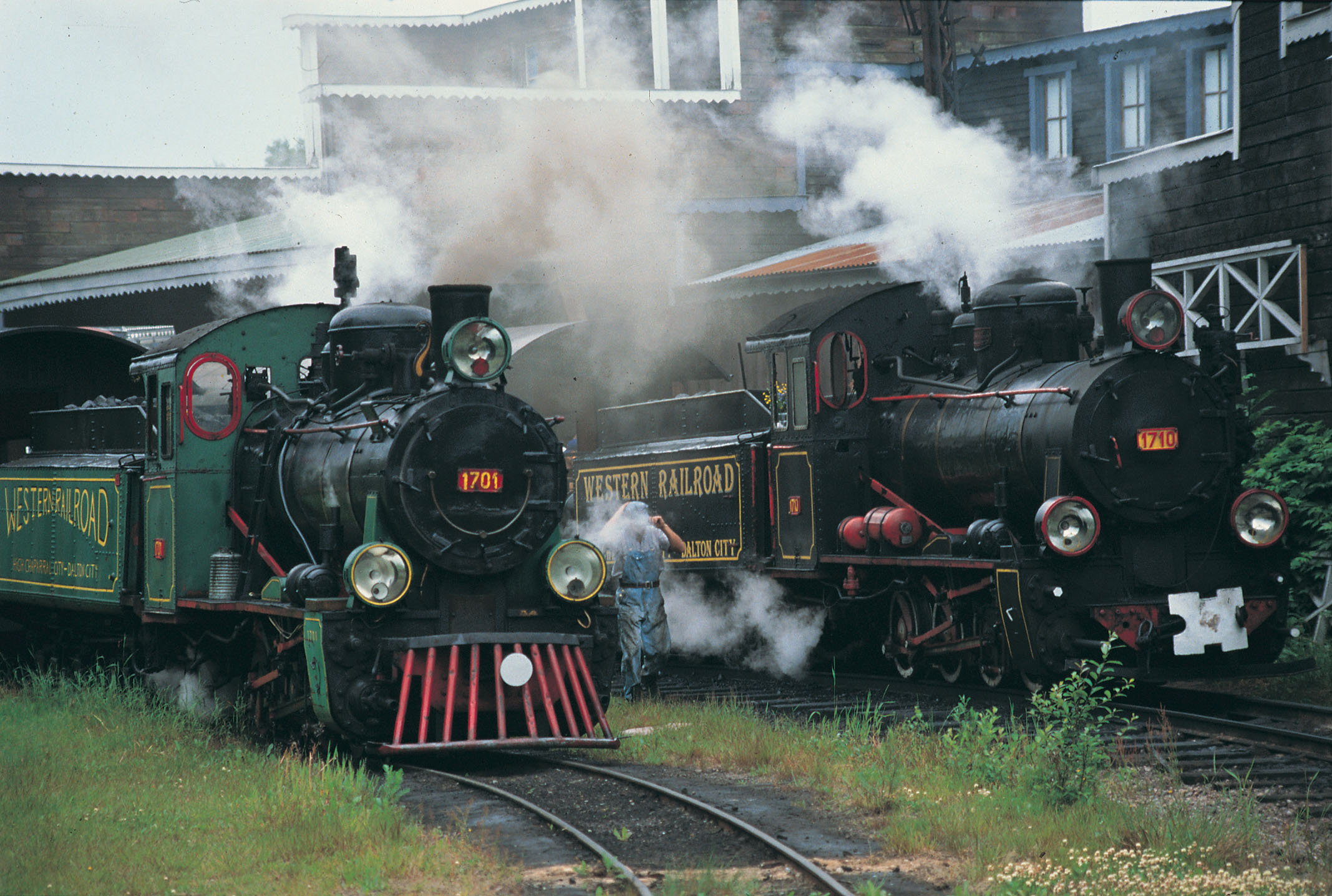 Man mellan två ånglok med påkopplade vagnar som tar besökare i Västern staden runt området