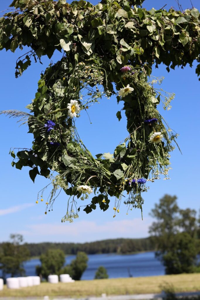 Midsommarstång med kransar vid Hestraviken, med Algustorpasjön i bakgrunden under midsommarlunchen.